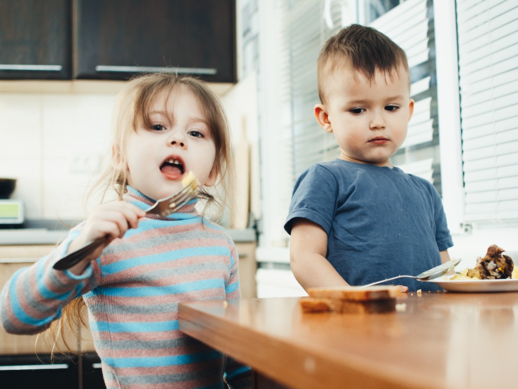 Los niños en la cocina comen carne y puré de papas, muy divertidos, comparten y se alimentan